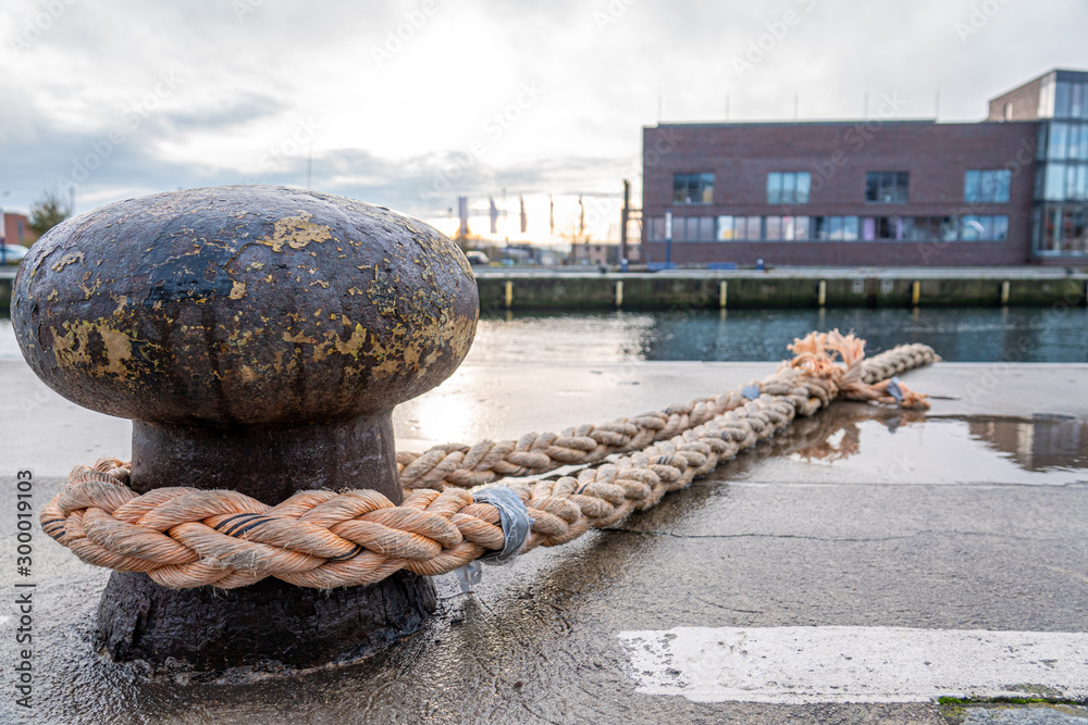a ship is attached with a thick rope to a bollard in the harbour