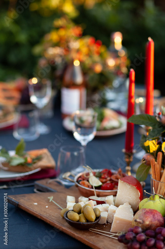 Dinner party outside to celebrate special occasion. Light snacks, fruit, cheese. Red candles as decor. Relax atmosphere, festive mood