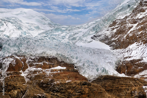 The Korola Glacier in Tibet covering the Himalaya Mountains, against a blue sky with white clouds. photo