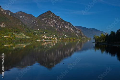Panoramic view of the mountains and Lake Idro. Autumn season, the reflection in the water of the mountains, trees, blue sky © Berg