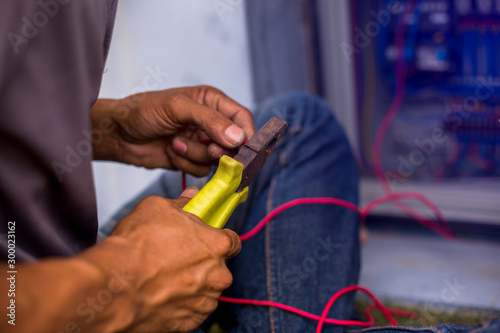 The electrician connected the electrical wires in the electrical control cabinet. The hands of the mechanic is carrying the tool into the electric wire.