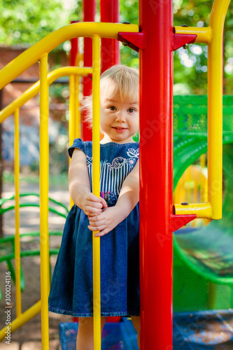 Child playing on outdoor playground. Little baby girl plays on school or kindergarten yard. Active kid on colorful swing.