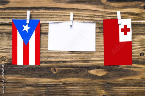 Hanging flags of Puerto Rico and Tonga attached to rope with clothes pins with copy space on white note paper on wooden background.Diplomatic relations between countries. photo