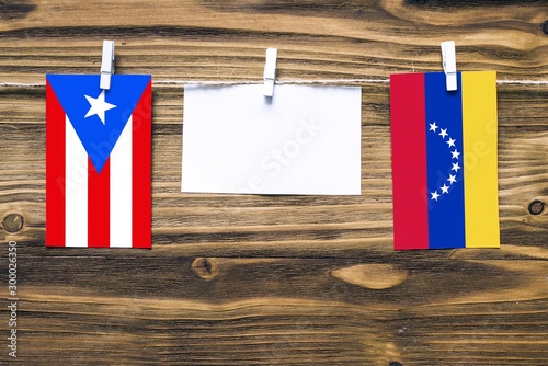 Hanging flags of Puerto Rico and Venezuela attached to rope with clothes pins with copy space on white note paper on wooden background.Diplomatic relations between countries.