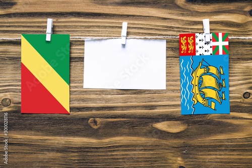 Hanging flags of Republic Of The Congo and Saint Pierre And Miquelon attached to rope with clothes pins with copy space on white note paper on wooden background.Diplomatic relations between countries.