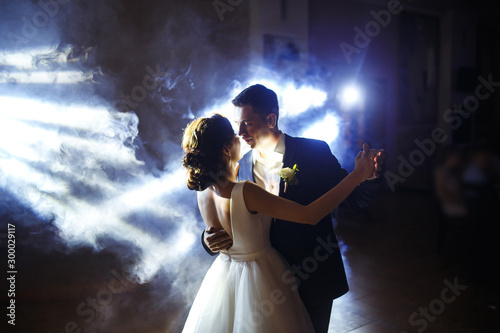 Fototapeta Naklejka Na Ścianę i Meble -  First wedding dance of newlywed. Wedding couple dancing in the darkness. Groom holds bride's hand dancing with her in the middle of a restaurant. Happy bride and groom and their first dance. 