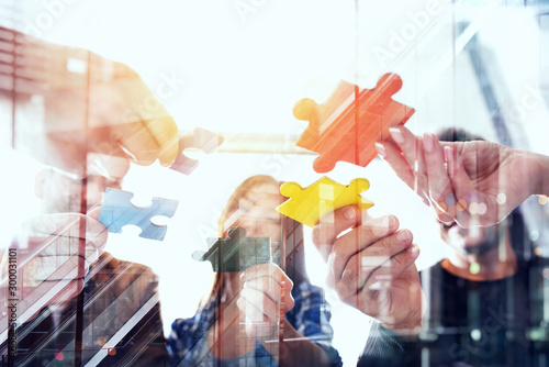 Business people join puzzle pieces in office. Concept of teamwork and partnership. double exposure with light effects