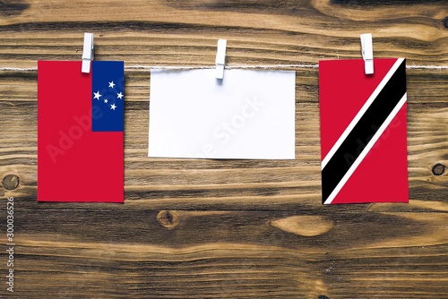 Hanging flags of Samoa and Trinidad And Tobago attached to rope with clothes pins with copy space on white note paper on wooden background.Diplomatic relations between countries. photo