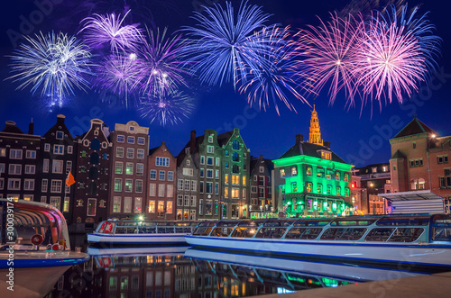 Traditional old buildings and boats with fireworks at night in Amsterdam, Netherlands.