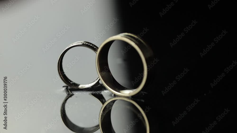 Wedding rings on black, white water surface. Groom ring rolling to bride's ring Wedding rings on black, white water surface. Groom ring rolling to bride's ring