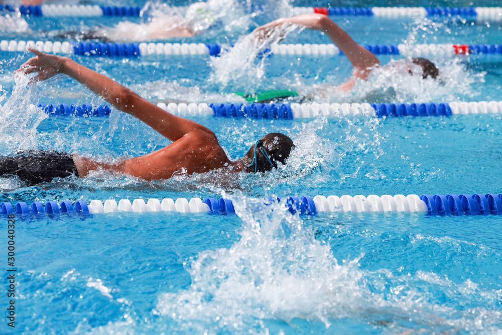 Motion blurred swimmers in a freestyle race, focus on lane line and water drops