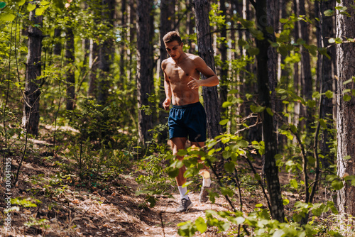 Man in sports wear running through the forest near the trees