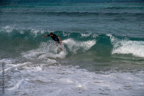 Young man riding a wave on a skimboard (a mix of surf and skate) in Cala Mesquida (Mallorca, Spain)
