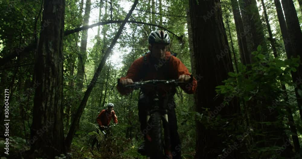 Close up of two men biking through forest in slow motion