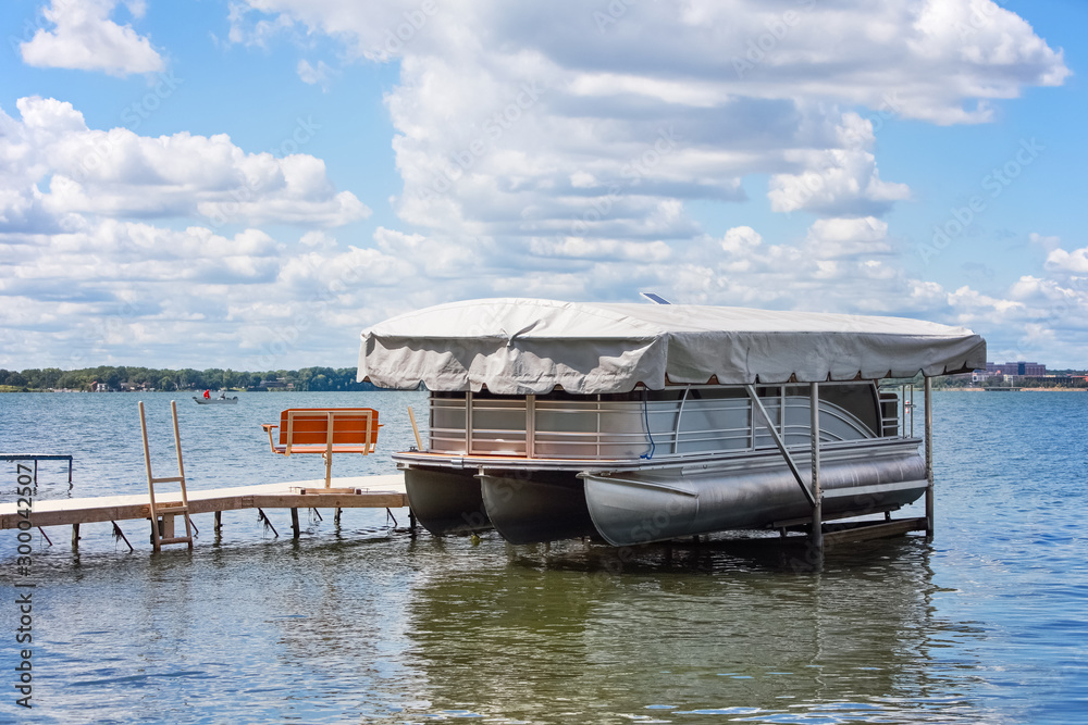 Pontoon boat with cover resting in boat lift on an inland lake Pontoon boat with cover resting in boat lift on an inland lake