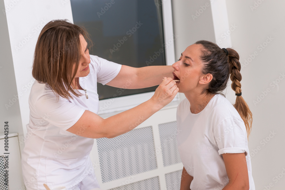 Obraz premium Female doctor checking a teenage girl's mouth with a depressor.