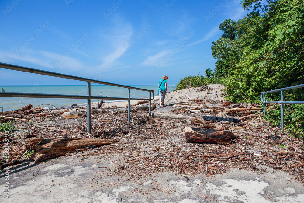 Woman walking at the beach on Lake Michigan, lake is covered in driftwood and debris from high water and storms