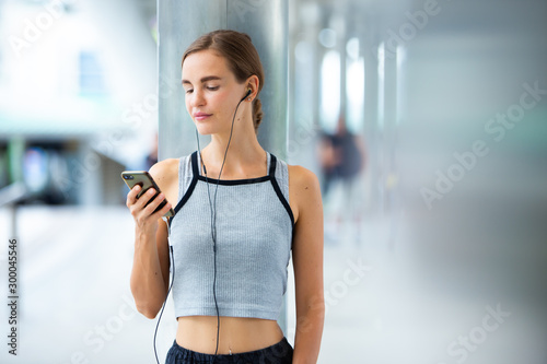 Portrait of fit and sporty young woman asian outdoors listening music using mobile phone. Fitness female looking relaxed in city