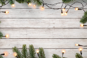 Christmas lights bulb and pine leaves decoration on white wood plank, frame border design. Merry Christmas and New Year holiday background. top view.
