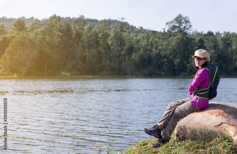 Backpacking Asian woman sitting on rock at outdoor,Happy and smiling,Camping hiking concept Backpacking Asian woman sitting on rock at outdoor,Happy and smiling,Camping hiking concept