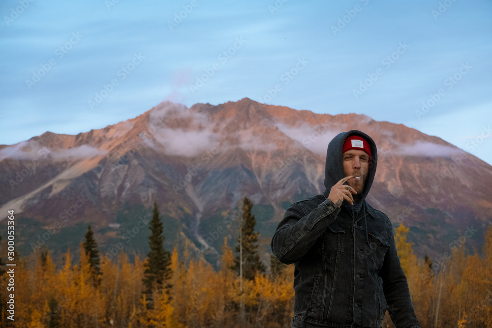 Young man in denim jacket smoking in nature during sunset