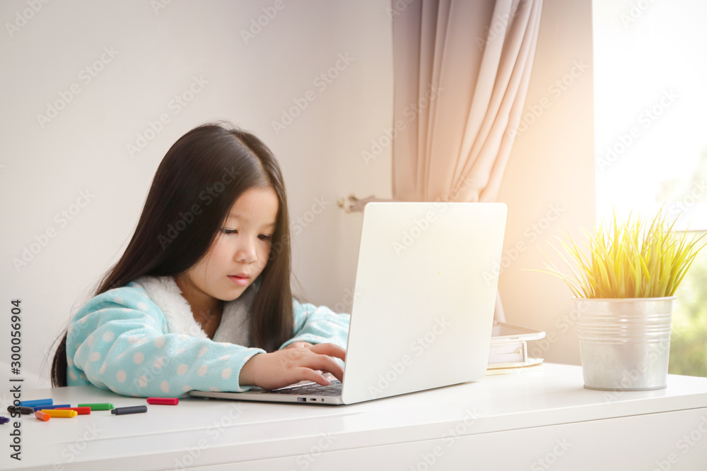 A little girl with long hair, watching online media, internet, in a notebook computer on a white table in her house A little girl with long hair, watching online media, internet, in a notebook computer on a white table in her house