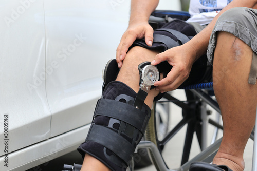 Senior man wear knee support brace on leg standing at the car parking lot  Medical and healthcare concept