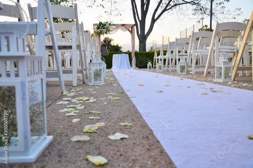 Fototapeta Naklejka Na Ścianę i Meble -  White cloth runner flanked by empty white chairs leading to a wedding altar