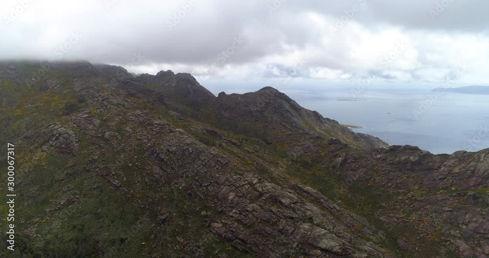 Aerial: Drone approaching clouds moving over rocky mountain by sea against sky - Galicia, Spain Aerial: Drone approaching clouds moving over rocky mountain by sea against sky - Galicia, Spain