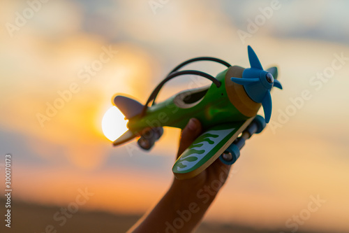 Boy's hand holds a wooden airplane against the sky during sunset. Close-up of a child's hand with a plane. Toy plane in the hand of a child of eight years. Freedom and happiness concept. photo