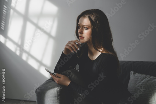 Portrait of a young sad crying girl with a smartphone in her hand.