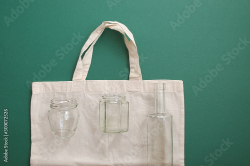 Reusable shopping bag and reusable glass bottles against the green background