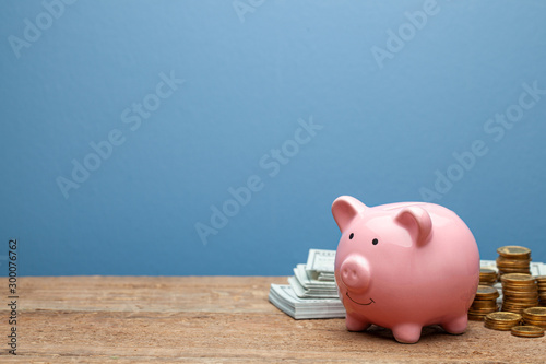 Fotografija Pink piggy bank and money with banknotes and coins on a wooden table and blue background