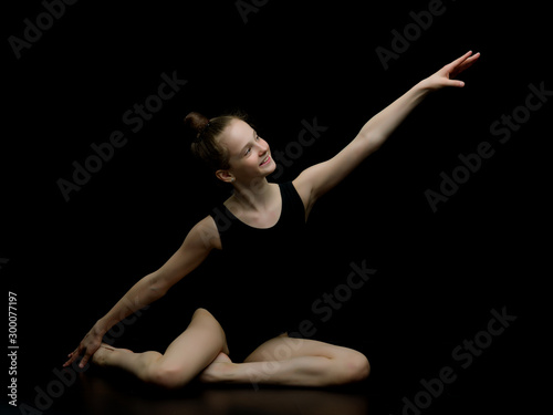 Girl gymnast in the studio on a black background performs gymnas photo