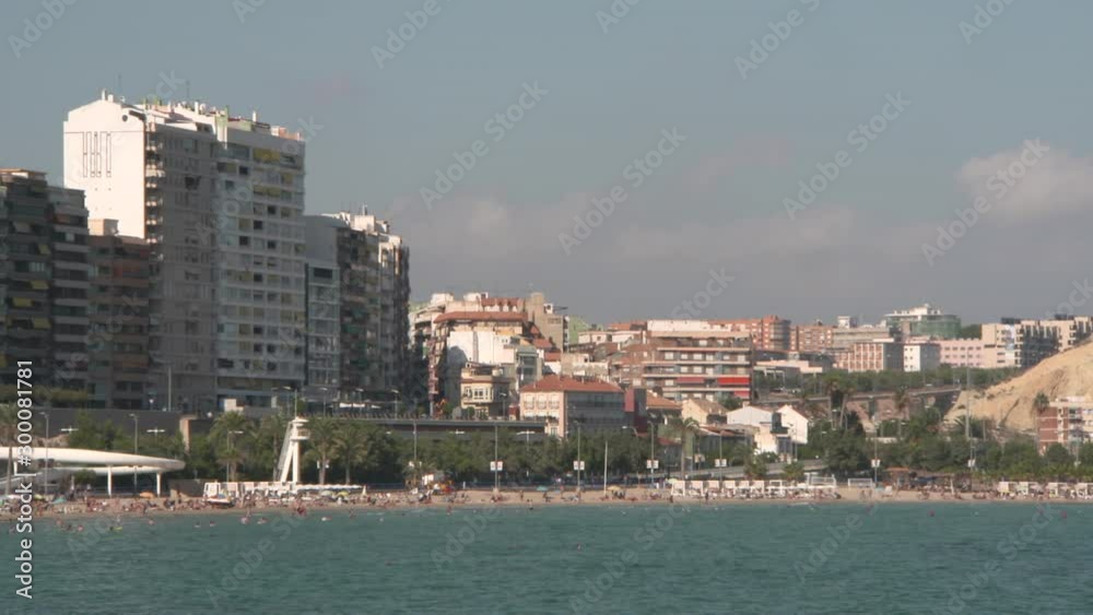 People enjoying at beach by buildings in city against sky on sunny day - Alicante, Spain People enjoying at beach by buildings in city against sky on sunny day - Alicante, Spain