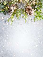 Christmas or winter background with a border of green and frosted evergreen branches and pine cones on a grey vintage board. Flat lay