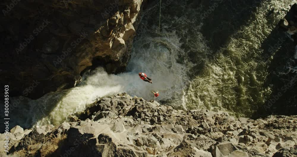 Two mountain climbers dangling off of ropes over a waterfall in the distance Two mountain climbers dangling off of ropes over a waterfall in the distance