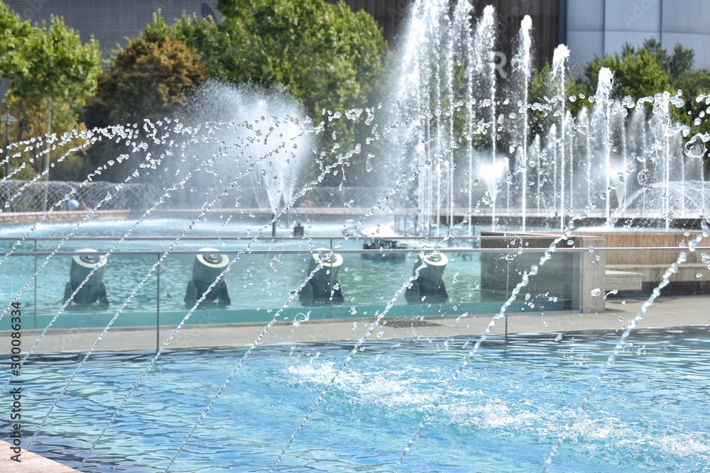 Spray fountain in the center of city with selective focus and blurred background. Running fountain with splashes and drops of water. Water jets in the fountain.