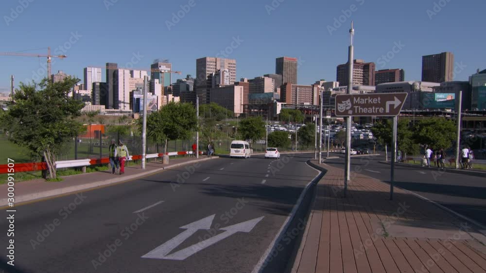 Vehicles on street by pedestrians walking against modern buildings in city against sky - Johannesburg, South Africa