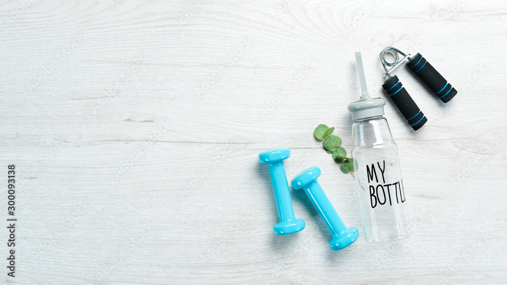 Fitness dumbbells, expander and water bottle. On a white wooden background. Flat lay. Fitness dumbbells, expander and water bottle. On a white wooden background. Flat lay.