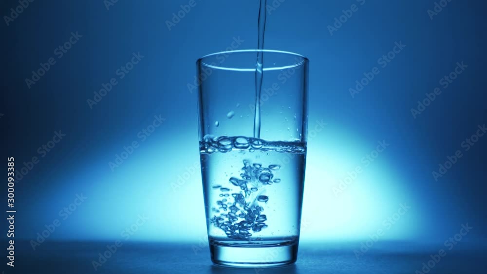 Pure clear water is poured into a glass on a blue background. Pure clear water is poured into a glass on a blue background.