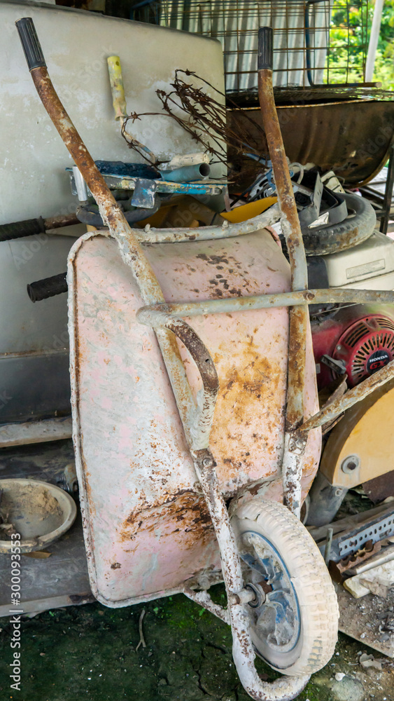 Fototapeta premium An old rusty 3-wheeled wheelbarrow leaning back at the storage place.