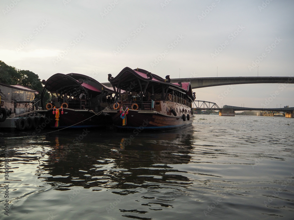 BANGKOK, THAILAND - OCTOBER 12, 2019: Tourist boat dock at a pier in Chaophraya river closed to a hotel and near a bridge in Bangkok. Cruises at Anantara Riverside Bangkok Resort at Sunset