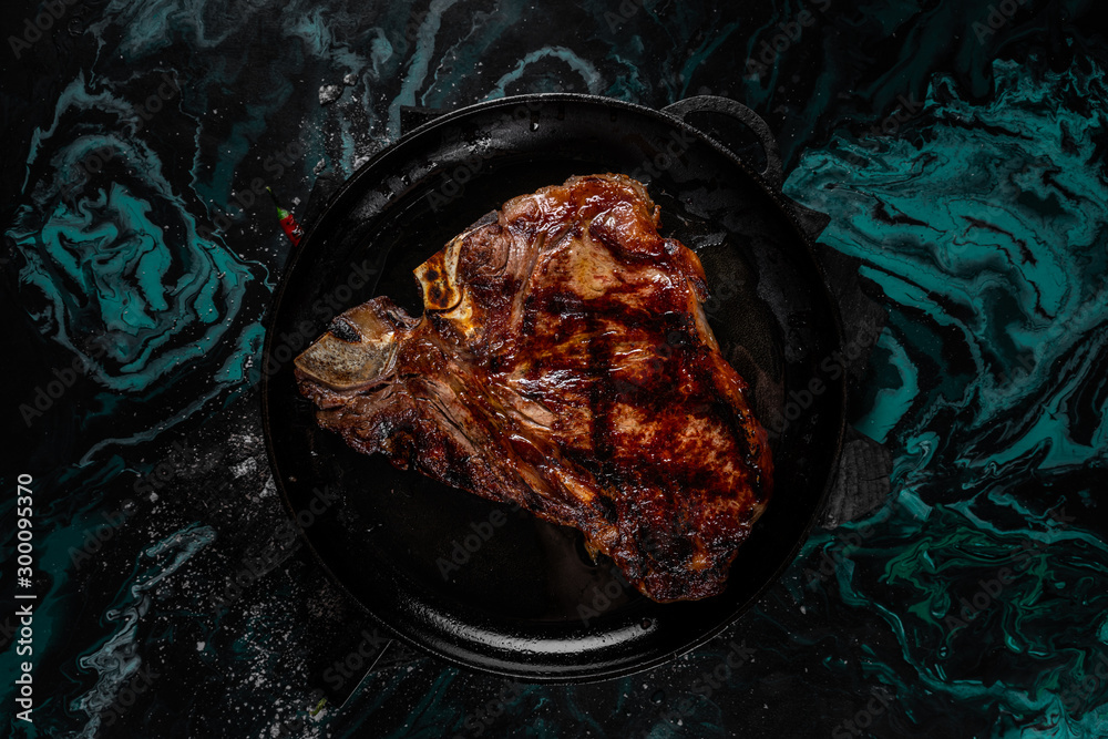 Fried meat steak on a black background of charcoal. Cooked juicy steak with smoke on the coals with rosemary. Grilled delicious marinated steak on coals, closeup photo. Fried meat steak on a black background of charcoal. Cooked juicy steak with smoke on the coals with rosemary. Grilled delicious marinated steak on coals, closeup photo.
