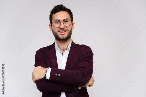 Men's fashion concept. Portrait of a handsome male model in glasses shows hands wearing a dark jacket, posing on a gray background. Black hair. Close Studio Shot