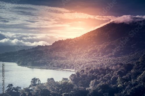 Beautiful Sunrise over Lake Buyan Bali Indonesia. Island Coastal Nature Exotic Landscape. Wonderful View on Green Bushes and Trees Forest Jungle, Mountain, Cloudy Sky and Sun Golden Rays
