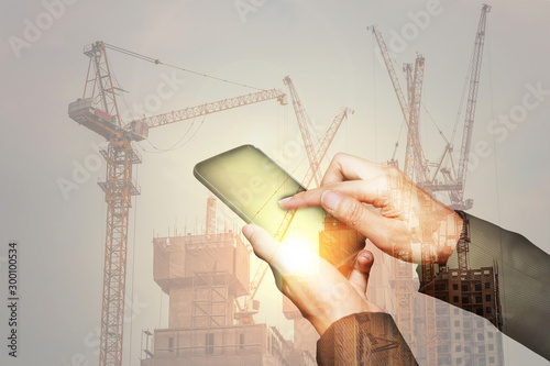 Double exposure of woman hand hold and touch screen smart phone, cellphone, construction crane, bulilding and sunlight of sunset as industry, business and high speed of communication concept. photo