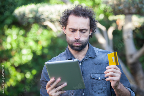 Frustrated buyer trying to pay online with credit card and a tablet outdoor
