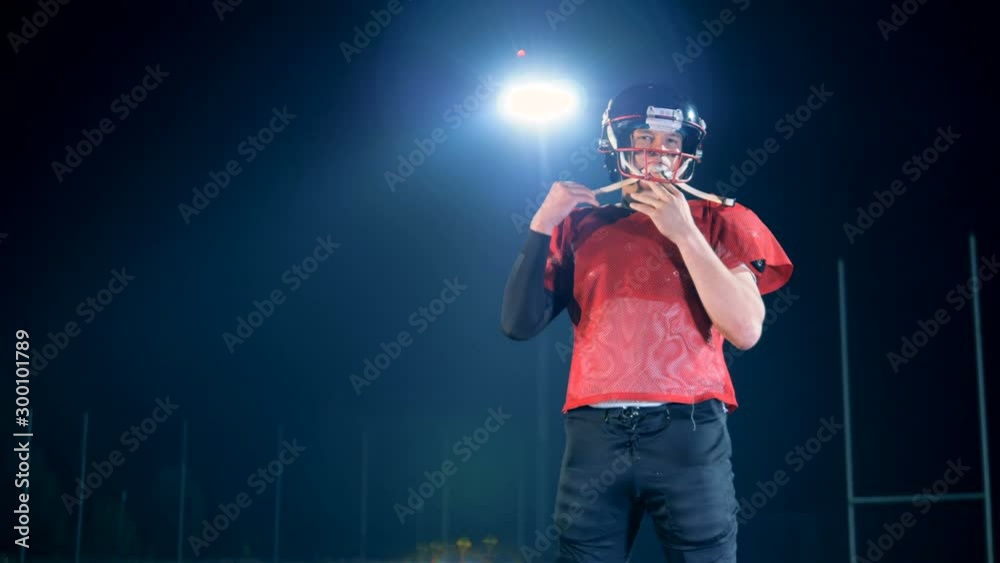 One footballer, american football player puts on a helmet, close up.