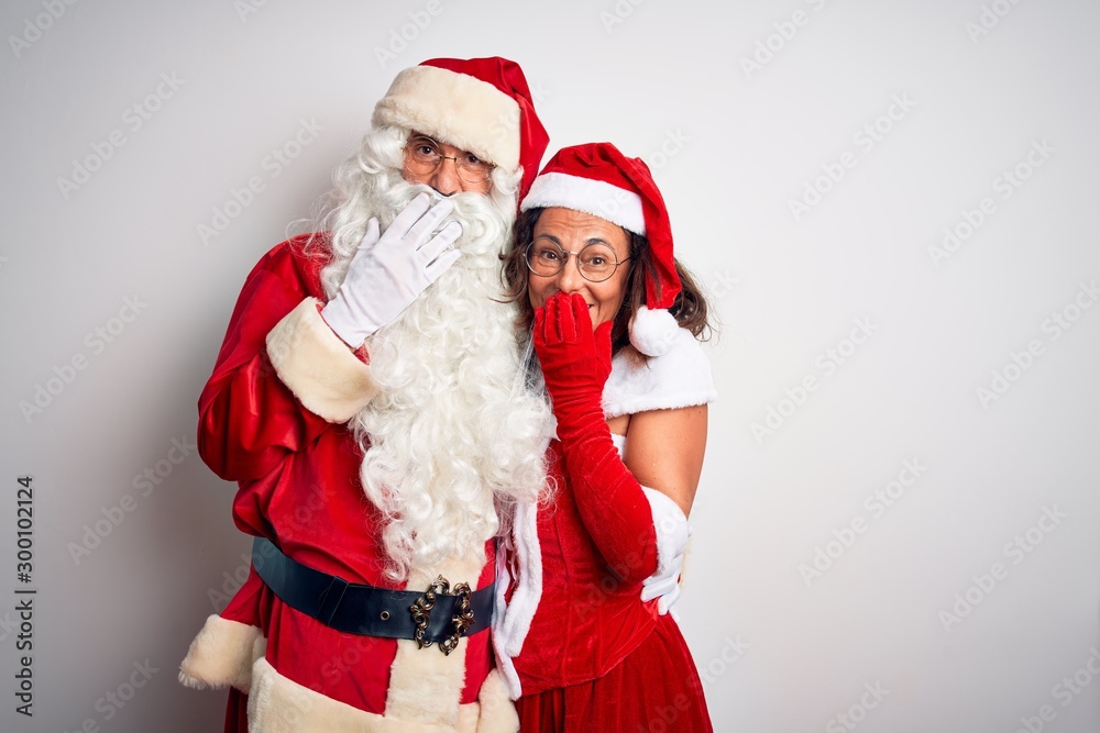 Middle age couple wearing Santa costume hugging over isolated white background laughing and embarrassed giggle covering mouth with hands, gossip and scandal concept Middle age couple wearing Santa costume hugging over isolated white background laughing and embarrassed giggle covering mouth with hands, gossip and scandal concept